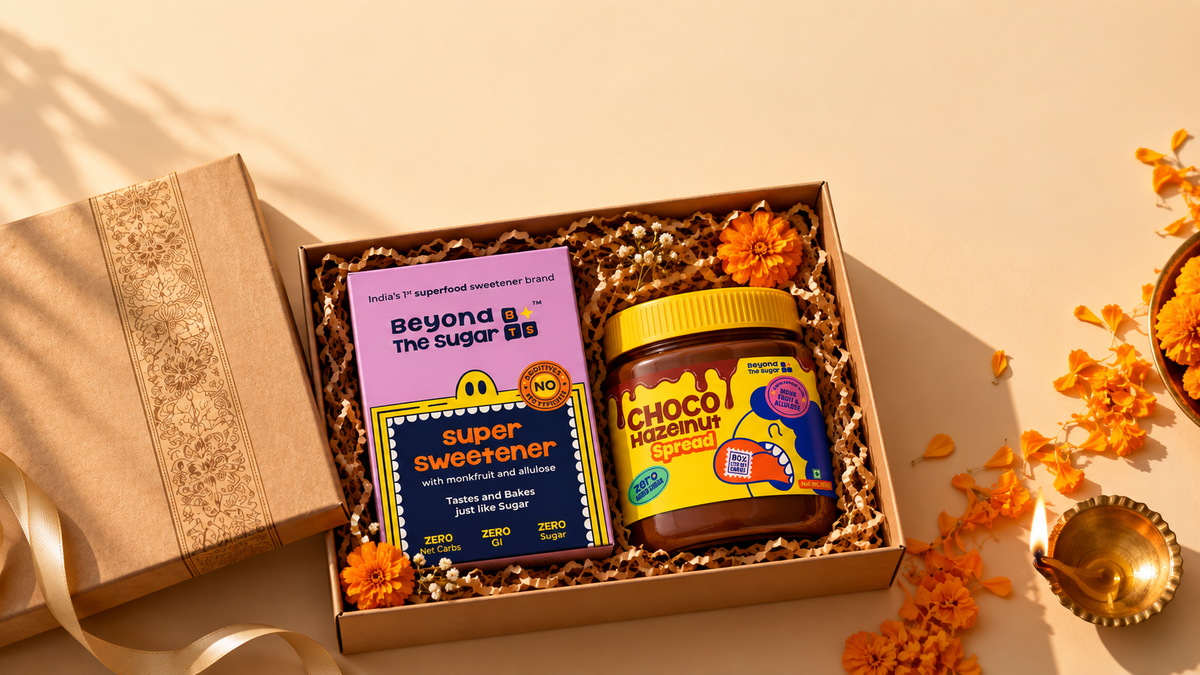 Sugar-free Diwali gift: a jar of Zero Added Sugar chocolate hazelnut spread and a monk fruit and allulose sweetener pouch in an open gift box beside a lit diya